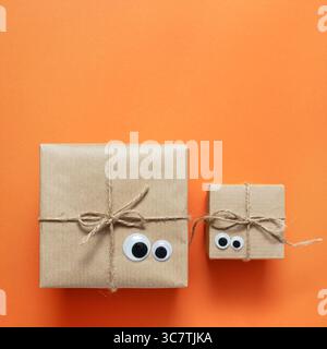 Card with brown craft gift boxes with eyes on orange background. Space for your text, square. Stock Photo