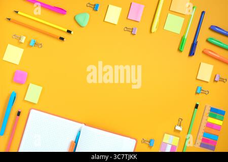 Frame of opened notebook and bright stationery on yellow background. Place for your text, flatlay. Stock Photo