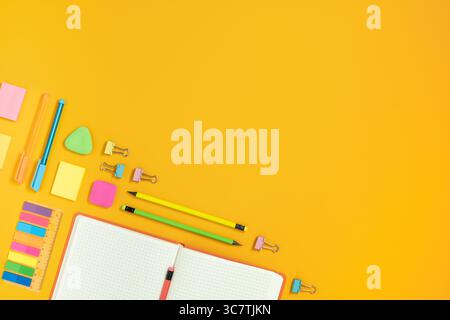 Frame of open notebook and colorful school and office stationery on yellow background. Flatly, copyspace. Back to school idea. Stock Photo
