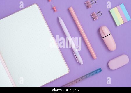 Empty notebook page for your text with pastel pink school and office stationery on violet background. Flatly. Stock Photo