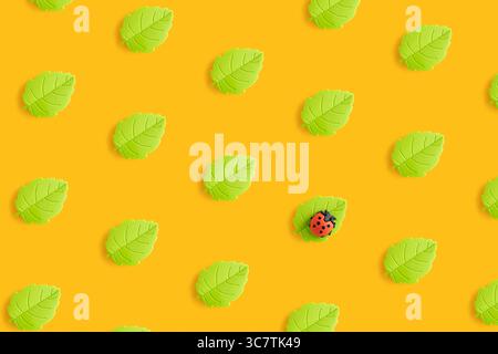 Toy ladybug on the leaf. Summer pattern of toy green leaves on yellow background. Stock Photo