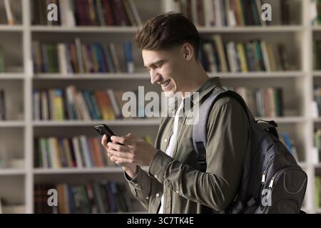 Gen z male student standing in library messaging on phone Stock Photo