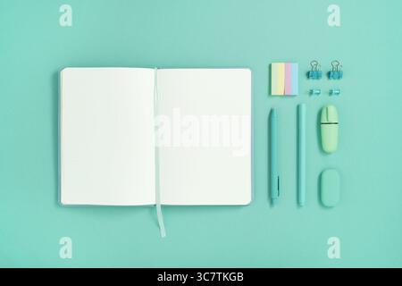 Open notebook with space for your text with green school and office stationery on turquoise background. Flatly. Stock Photo