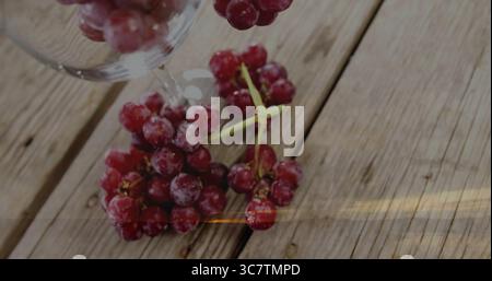Showing frosted red grapes resting on rustic wooden tabletop, under inverted clear wine glass Stock Photo