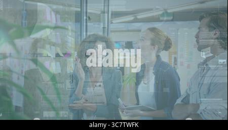 Brainstorming three professionals in office attire annotating glass in workspace with sticky notes Stock Photo
