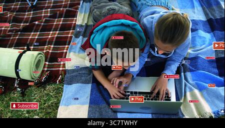 Using silver laptop on striped blue blanket in park, siblings checking subscribe and play icons Stock Photo