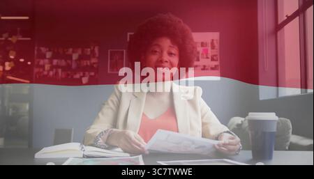 Holding printed picture designer in cream blazer at office desk, with coffee cup notebook pinboard Stock Photo