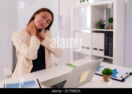 Asian business woman adult office worker experiencing neck discomfort while using laptop computer at corporate desk Stock Photo