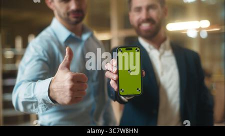 Caucasian men using mobile phone in office business app co-workers male guys smiling businessmen holding smartphone chroma key green screen mockup Stock Photo