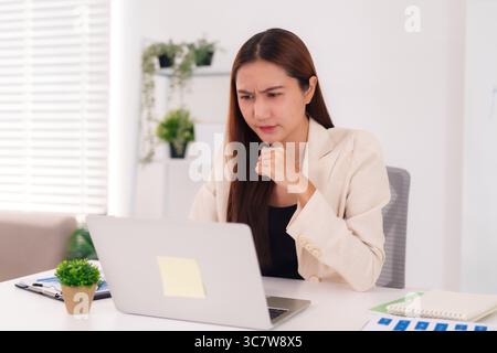 Asian adult businesswoman focused intently working on a laptop in a bright modern office She is contemplating a serious business challenge Stock Photo