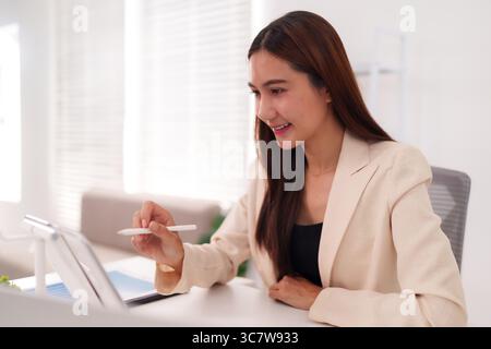 Asian female executive efficiently managing online business projects on a portable device fostering innovation and success Stock Photo