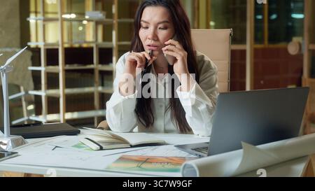 Asian business woman designer architect planner businesswoman talk mobile phone in office Chinese Korean Japanese girl organizer consulting client Stock Photo
