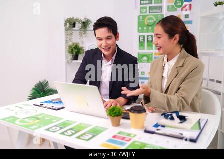 Asian adult professionals discuss ESG strategy analyze sustainable business data collaborate on corporate growth project in modern office setting Stock Photo
