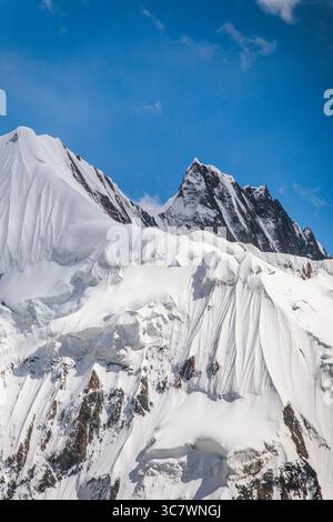 A vertical shot of steep snowcapped mountain peaks with rugged, rocky faces under a clear blue sky Stock Photo