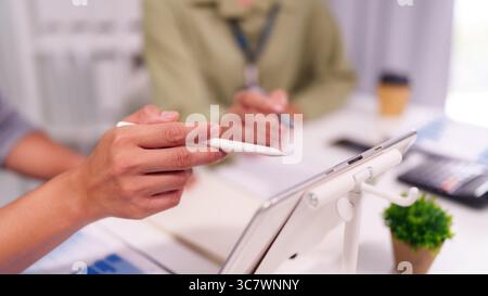 Focused team collaboration on a tablet in a modern office. Professionals analyze data plan strategies discuss business growth. Stock Photo