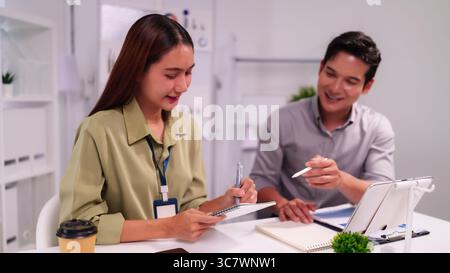 Two Asian colleagues actively engaging in a productive work meeting exchanging ideas and reviewing business plans for success Stock Photo