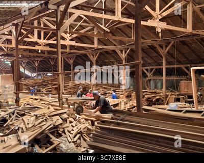 Badung, Bali, Indonesia – July 29, 2025: Carpenters cutting, sorting, and processing timber planks and boards in a traditional wood workshop Stock Photo