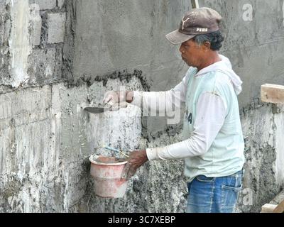Badung, Bali, Indonesia – August 1, 2025: Construction worker applying cement plaster on a concrete wall using a trowel and mixed mortar Stock Photo