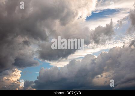 Dark and heavy storm clouds with patches of blue sky and warm light breaking through at sunset. A powerful natural sky scene full of contrast and move Stock Photo