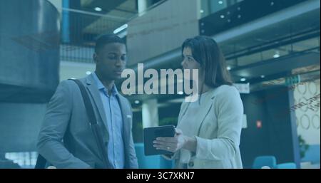 Man and woman in formal attire reviewing on tablet computer in corporate lobby, with shoulder bag Stock Photo