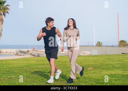 Fit couple jogging together on seaside lawn, smiling and chatting Stock Photo
