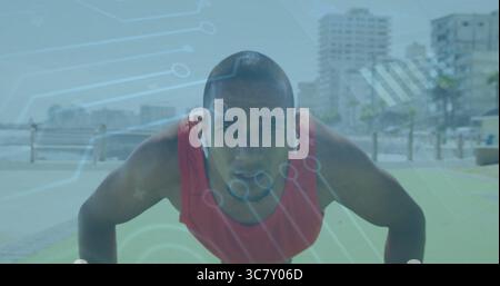 Doing push-ups adult man wearing red athletic top on seaside promenade, with green mat and earbuds Stock Photo