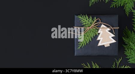 Black craft gift box with paper tree and cedar tree branches on dark background with space for your text Stock Photo