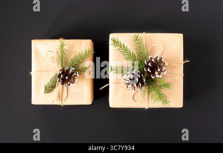 Two gifts in craft paper with a spruce branch and cones on a black background top view Stock Photo
