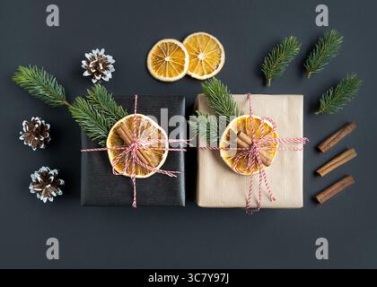 Two craft gift boxes decorated with oranges, spruce branches and cinnamon on a dark background. Gift packaging idea, diy. Top view. Stock Photo