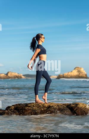 fit woman doing stretching exercises on rocks by the sea Stock Photo