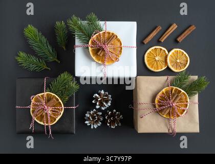 Three craft gift boxes decorated with oranges, spruce branches and cinnamon on a dark background. Gift packaging idea, diy. Top view. Stock Photo