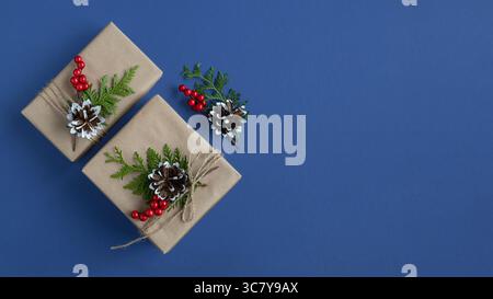 Banner with craft gift boxes with cones, thuja and berries on a blue background. Top view. Copyspace. Stock Photo