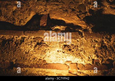 A section of old brick and stone wall is bathed in golden artificial light, revealing aged textures and masonry detail. Stock Photo