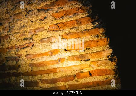 Old red bricks arranged in diagonal lines glow under a directional spotlight inside an aged architectural structure. Stock Photo
