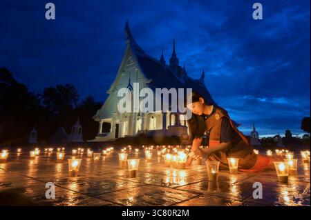 Young woman in traditional Thai clothing sitting outside a temple lighting candles, Thailand Stock Photo