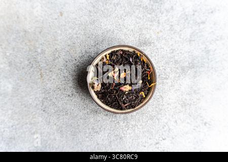 Overhead view of a bowl of black tea leaves with dried fruit and flowers on a grey kitchen worktop Stock Photo