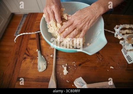 Close-up overhead view of a senior woman standing in a kitchen mixing cookie dough with her hands Stock Photo