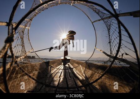 Rear view silhouette of a Traditional Intha fisherman standing in a boat on Inle lake, Myanmar Stock Photo