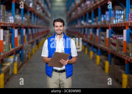 Warehouse worker checking stock levels on shelving racks in aisle, holding clipboard and pen Stock Photo