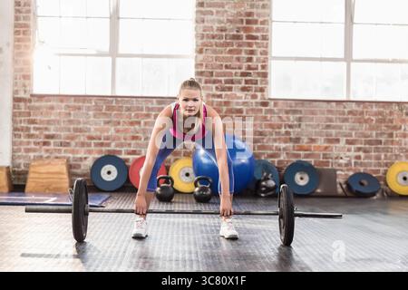 Female athlete lifting loaded barbell on rubber gym floor with kettlebells and stability ball Stock Photo