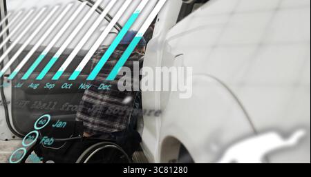 Man in wheelchair wearing plaid shirt and beanie inspecting car door in garage, featuring bar chart Stock Photo