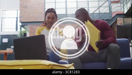 Reviewing printed charts coworkers wearing shirts on blue sofa in lounge, with mug yellow folders Stock Photo