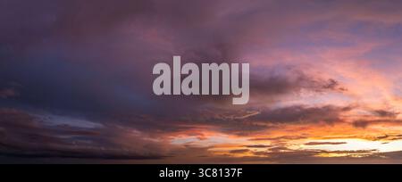 Bright sunset over dark rural land. Setting sun behind vivid orange and yellow clouds Stock Photo