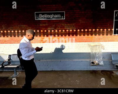 A man with a backpack looking at his smartphone and texting while walking at Bellingham station Stock Photo