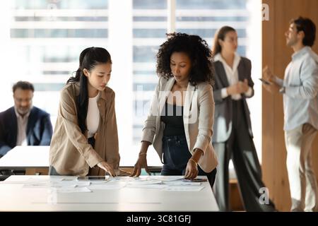 Two young female colleagues review paper documents on office desk Stock Photo