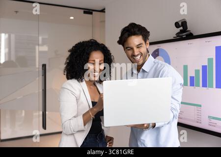 Two happy young businesspeople standing in conference room using notebook Stock Photo
