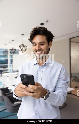 Happy millennial male manager using smartphone in modern office boardroom Stock Photo