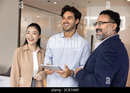 Successful smiling diverse multiethnic business partners looking aside using tablet Stock Photo