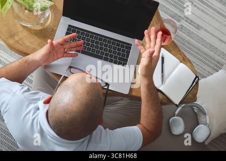 Man working from home, using laptop and smartphone while sitting on a comfortable sofa Stock Photo