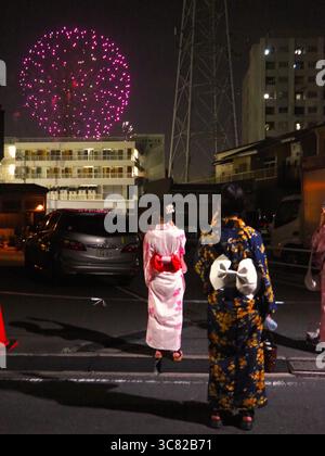 Women in yukata watching fireworks over buildings at night during Tokyo’s Itabashi Fireworks Festival Stock Photo